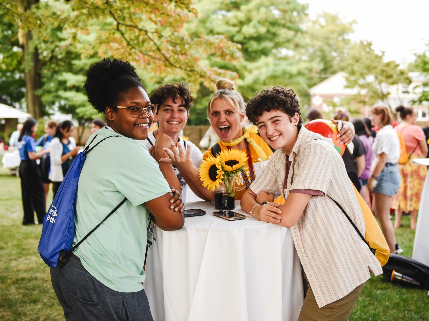 A group of students gather around a table outdoors during an orientation gathering.